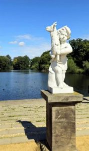 Eine weiße Statue eines Kindes mit einem Fisch am Ufer eines Sees im Schloss Charlottenburg, Potsdam.