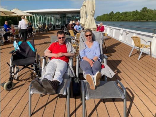 Ein Mann und eine Frau sitzen in Liegestühlen auf dem Deck eines Schiffes und genießen die Aussicht auf das Wasser.