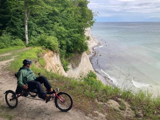 Eine Person genießt eine Radtour auf einem Liegerad entlang einer malerischen Küstenstraße mit Blick auf das Meer.