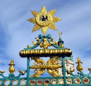 Detailansicht der prunkvollen Verzierungen am Eingangstor des Schlosses Charlottenburg in Potsdam. Goldene und grüne Elemente dominieren das Bild.