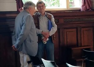 Zwei Männer stehen in einem Raum mit Holzwänden und unterhalten sich.